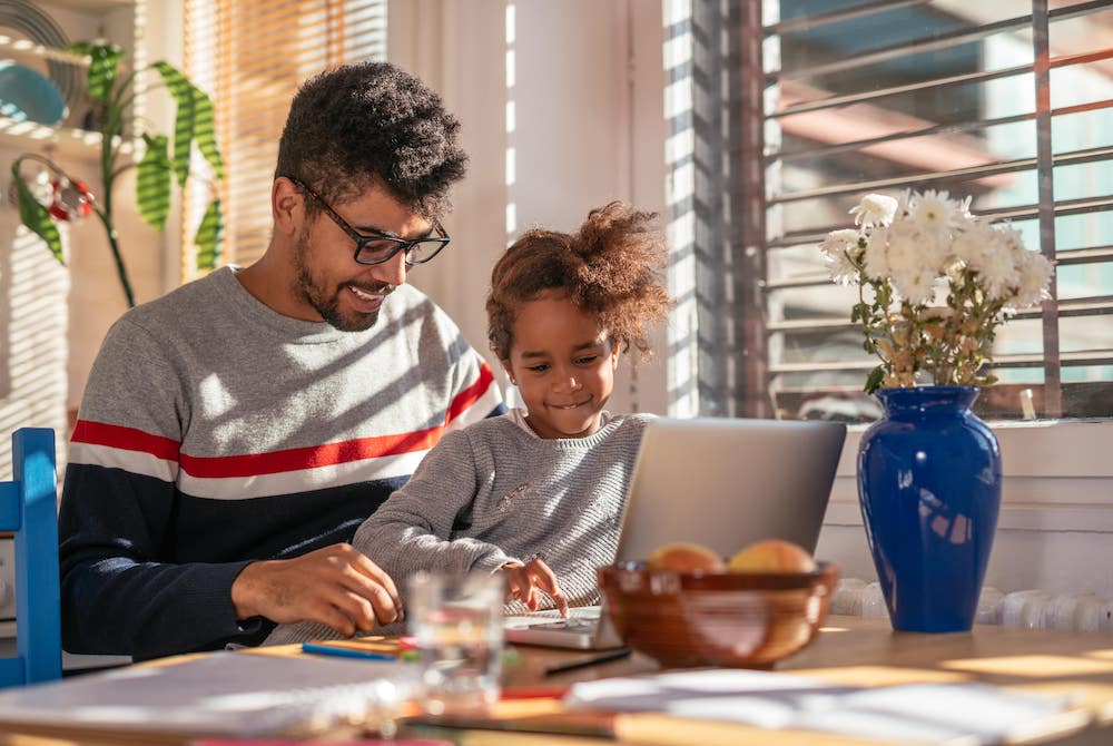 Father working on his laptop in the kitchen while spending time with his daughter
